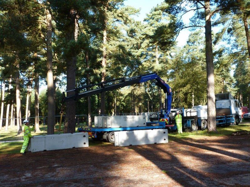 Lorry mounted crane unloading concrete barriers in a wooded parkland setting