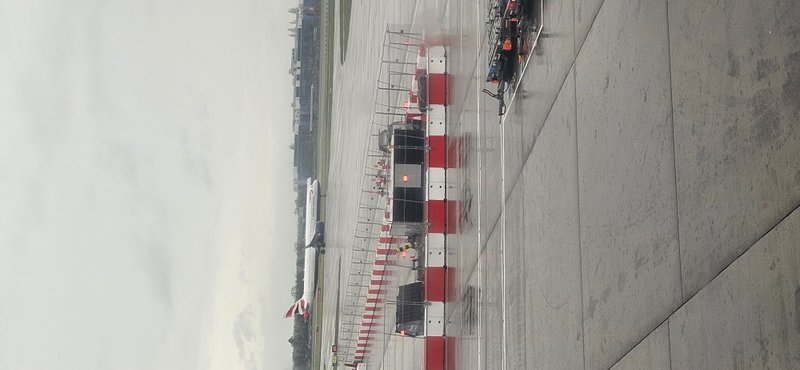 Red and white temporary vertical concrete barriers topped with mesh fencing across a wide concrete apron