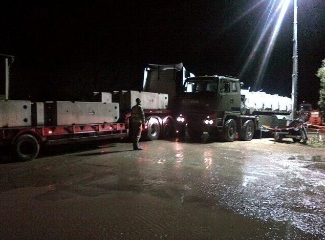 Barriers delivered at night beside a military truck on flooded ground