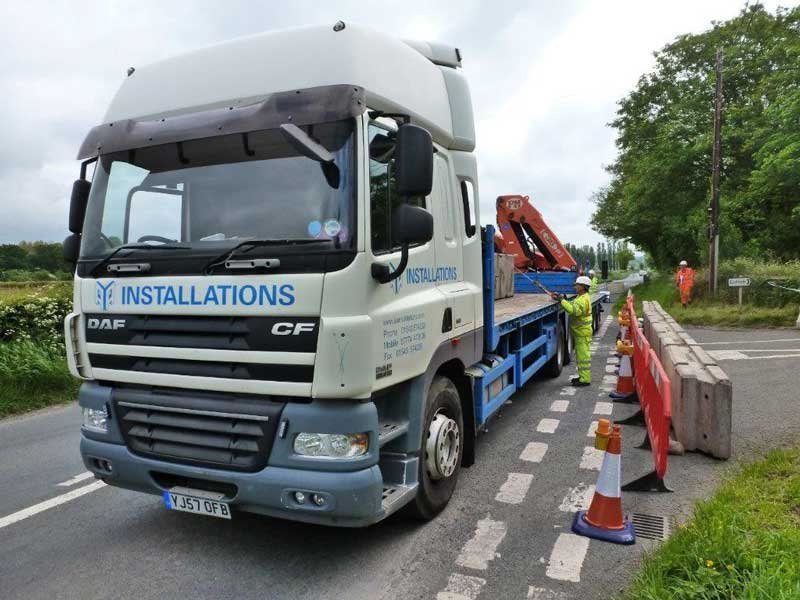 Crane lorry delivering TVCB barriers to a coned-off roadside