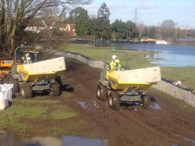 Site dumpers carrying concrete barriers along a riverside flood embankment