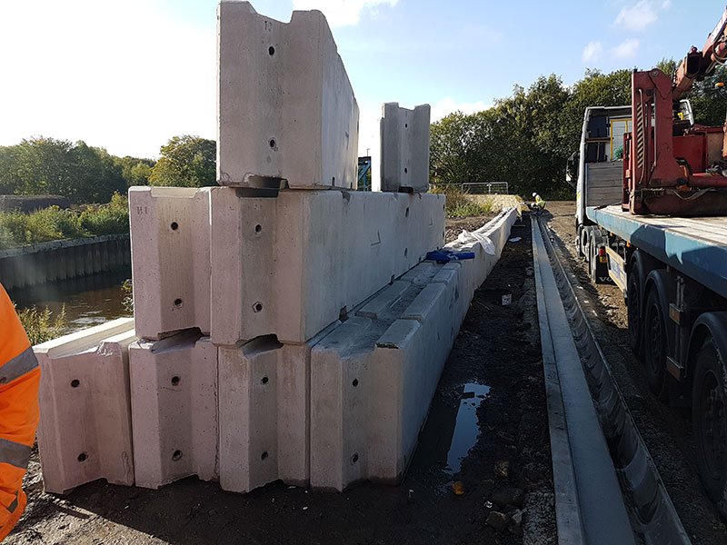 Stacked concrete barrier units beside a canal towpath awaiting installation