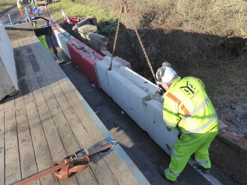 Worker guiding a concrete barrier lowered on chains onto a bridge deck