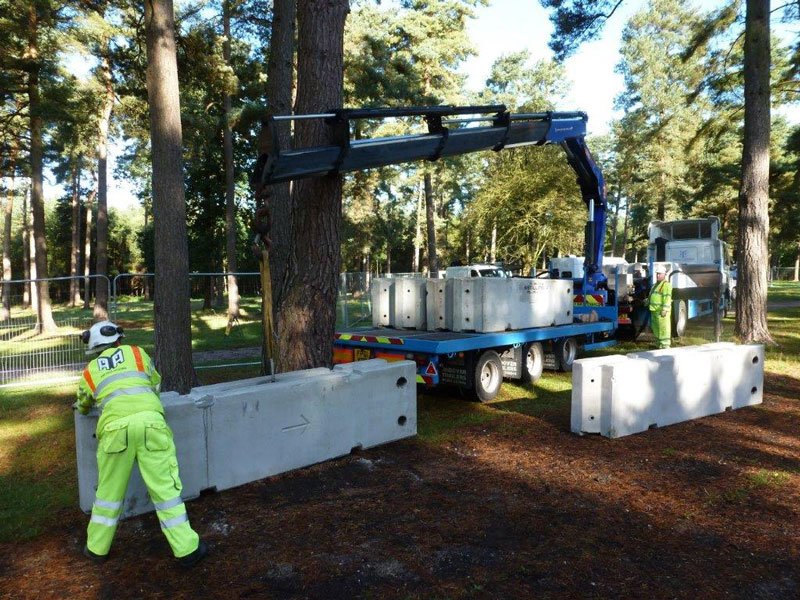 Operative guiding a TVCB barrier lifted from a crane lorry in woodland