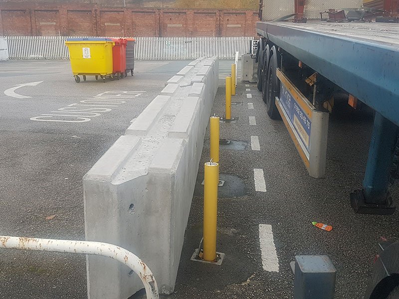 Concrete barrier and yellow bollards separating a car park from a parked trailer