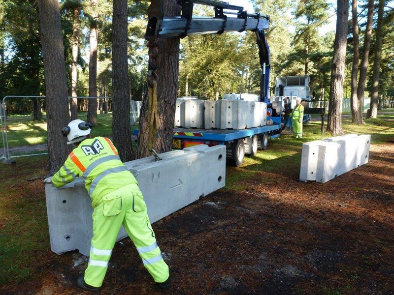 Hi-vis operative positioning a TVCB barrier beside a crane lorry in woodland