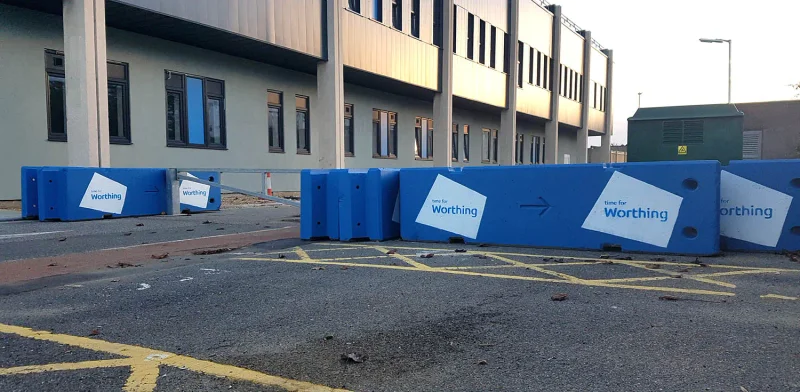 Blue Worthing-branded concrete barriers separating a car park outside an office building