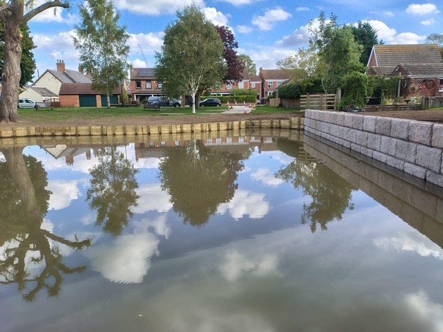 Rock-faced Vee-Rock retaining wall lining the bank of a flooded pond beside houses