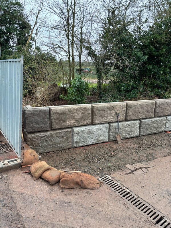 Small two-course Vee-Rock retaining wall beside a metal gate and drainage channel
