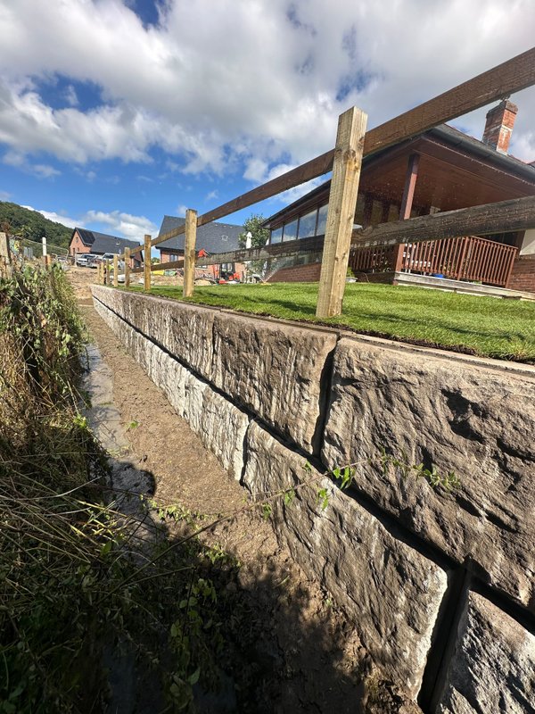Rock-faced Vee-Rock retaining wall holding a grassed bank beside a timber-clad building