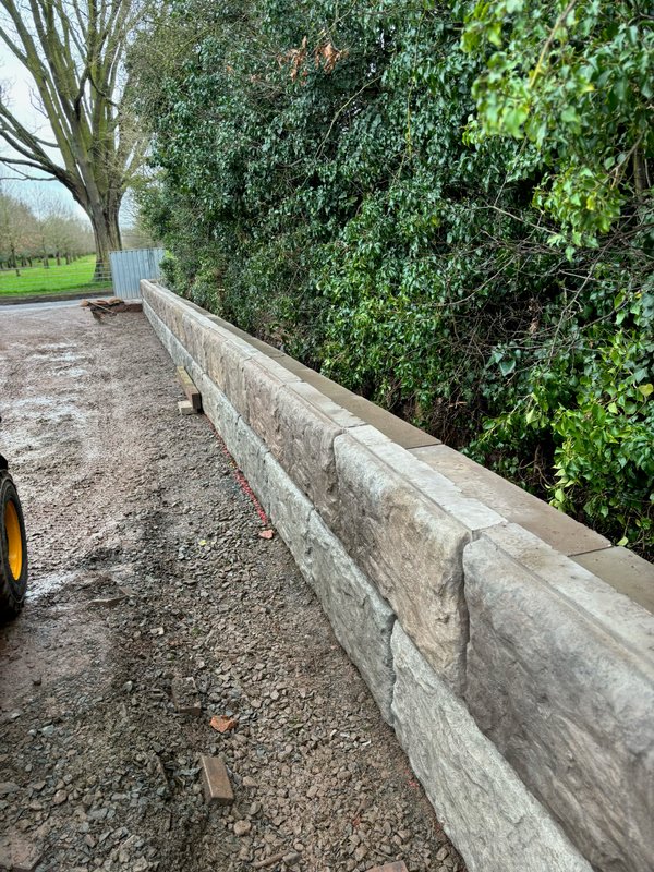 Rock-faced Vee-Rock retaining wall running along a new driveway below a wooded bank
