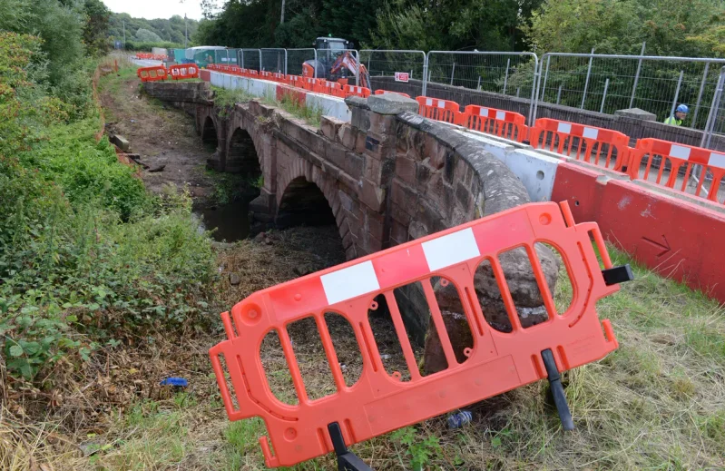 Barriers and fencing lining a stone arch bridge closed for repair works
