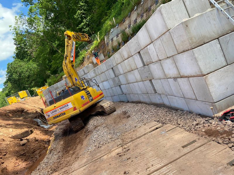 Tracked excavator working beside a tall curved interlocking block wall