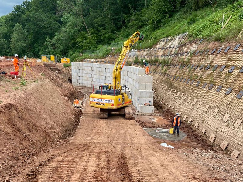 Excavator placing interlocking blocks in a deep excavation below a nailed slope
