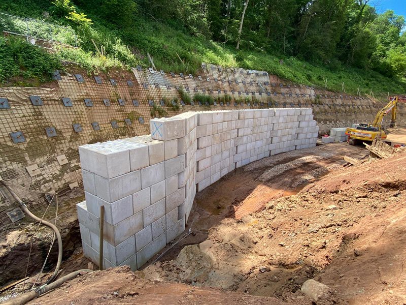 Curved Legato block wall rising from an excavation below a meshed slope