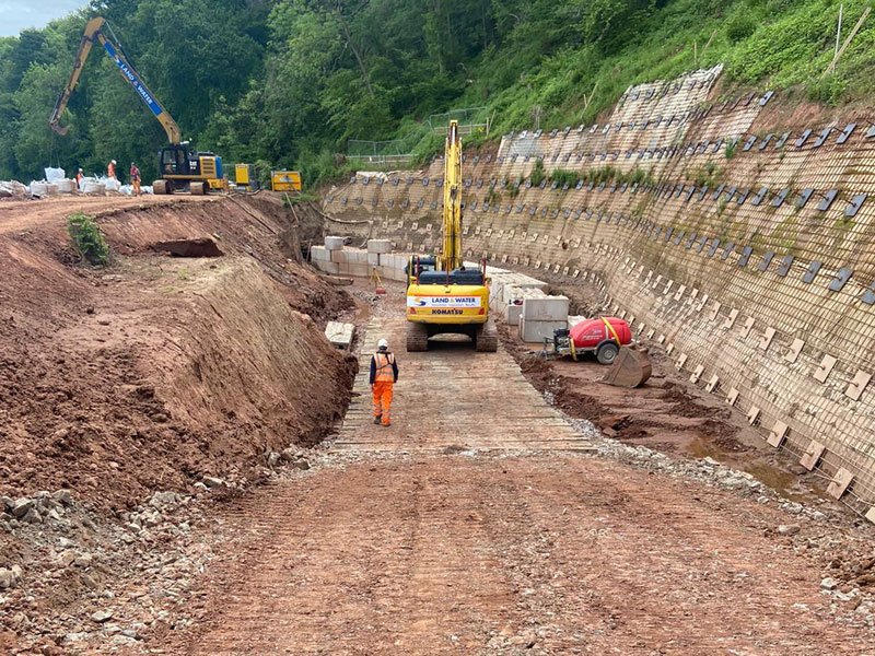 Excavator working a deep channel excavation between block-faced retaining walls
