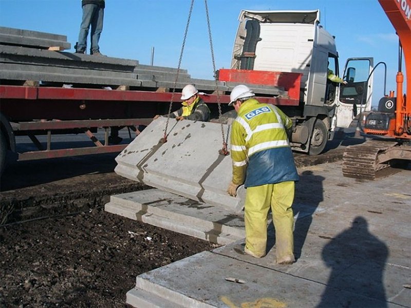 Worker guiding a precast utility protection slab lowered on chains into a trench