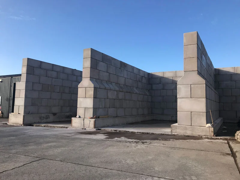 Tall material storage bays formed from grey interlocking blocks under clear blue sky
