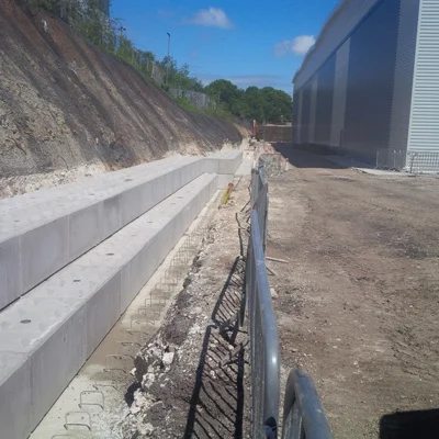 Legato block base walling retaining an excavated slope alongside a large industrial building