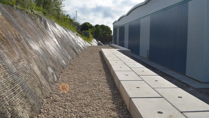 Legato block retaining wall running alongside a steep meshed embankment and industrial unit