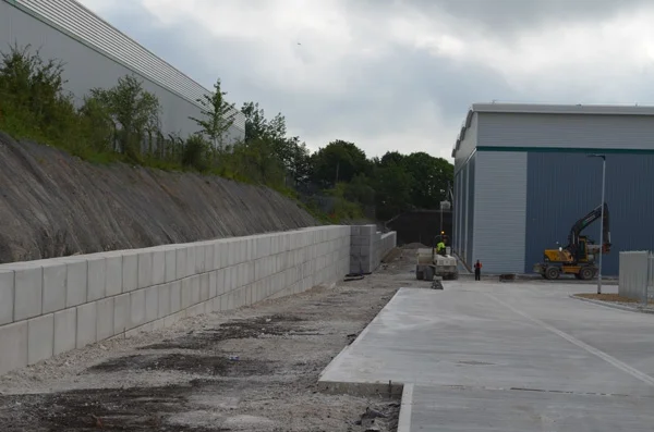 Interlocking block retaining wall holding an earth bank beside a new industrial yard