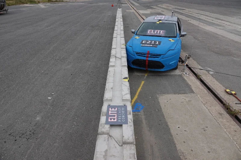 Blue test car alongside a run of concrete barriers on a test track