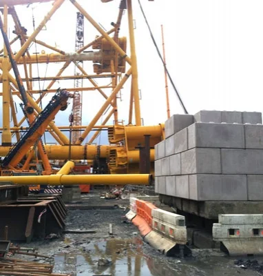 Concrete counterweight blocks stacked beside crane rigging on a wet working site