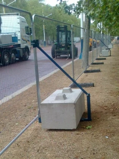 Concrete ballast blocks weighting a run of temporary fencing along a roadside