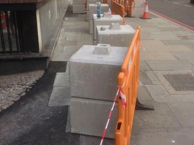 Kentledge blocks weighting orange pedestrian barriers along a city pavement