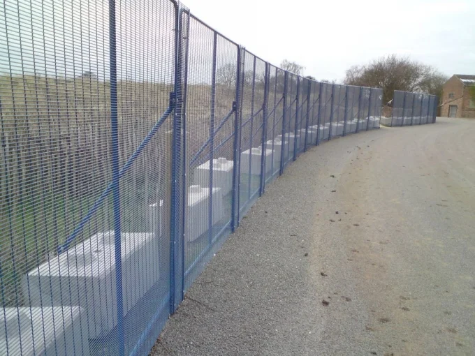 Mesh security fencing along a trackside path supported on kentledge ballast blocks