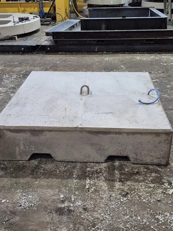 Flat precast concrete ballast block with a lifting eye resting on rough ground
