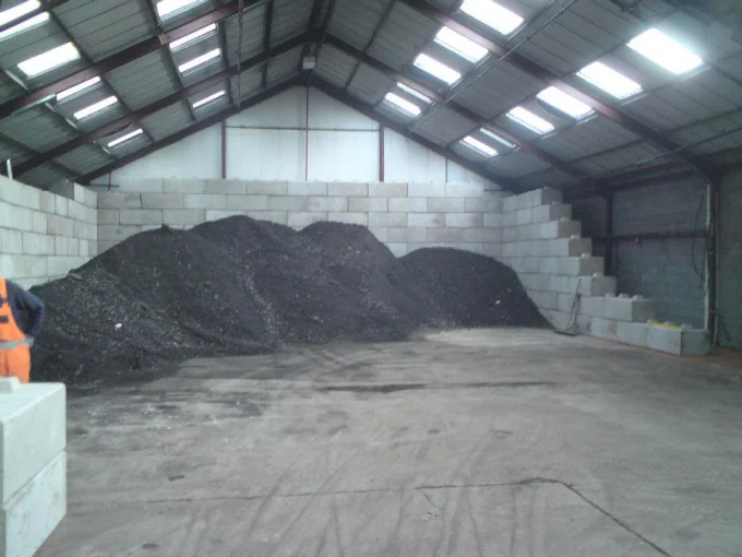 Interlocking concrete block walls containing a black asphalt stockpile inside a storage shed