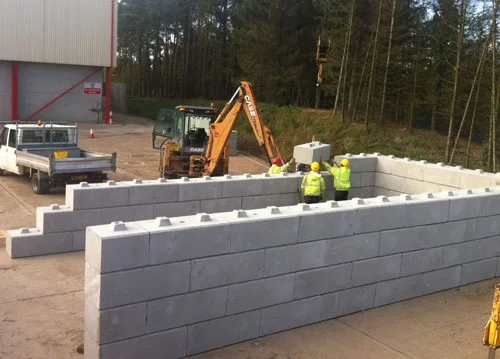 Duo blocks being craned into place to form a bunker wall outside a warehouse