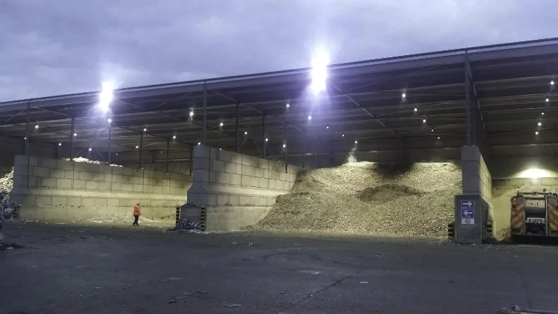 Floodlit covered storage bays holding heaps of aggregate behind interlocking block walls