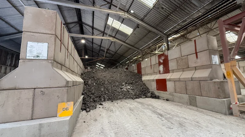 Interlocking concrete blocks forming storage bays holding heaped dark aggregate inside a shed