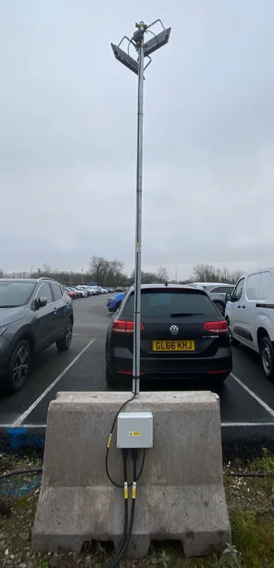 Jersey barrier anchoring a car park lighting column with a control box attached