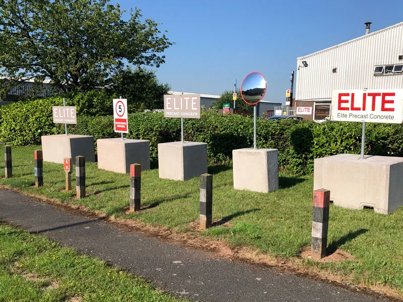 Concrete counterweight blocks on a grass verge holding signage posts without drilling