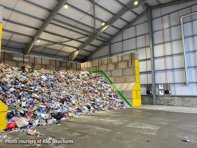 Mixed waste piled against a Legato block push wall inside a recycling shed