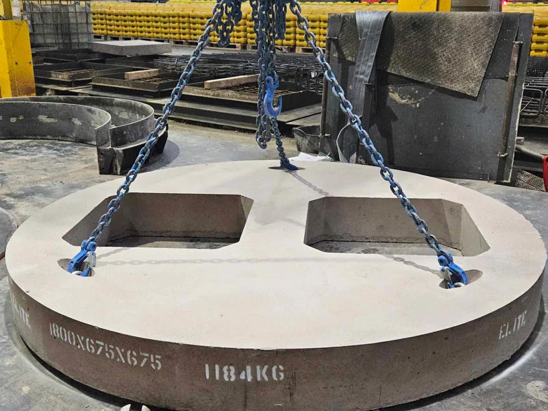 Circular bespoke concrete cover slab lifted on chains in the casting yard, weight marked