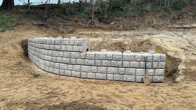 Curved cobblestone-finish retaining wall newly installed in a sandy excavation