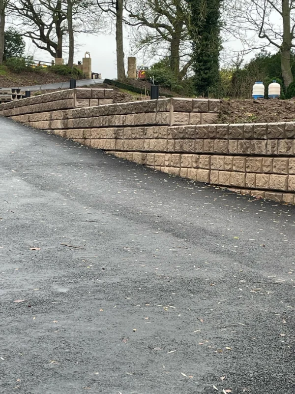 Cobblestone-finish Retainer-Rock retaining wall curving alongside a newly surfaced access road