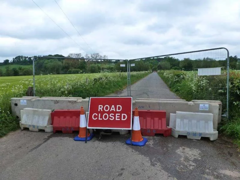 Concrete barriers and cones closing a country lane behind a Road Closed sign