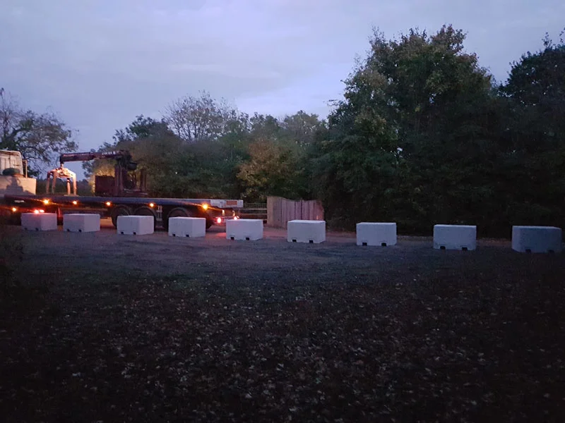 Line of concrete security blocks spaced across a gravel compound at dusk