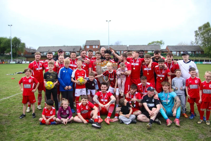 Football club squad of adults and children posing with a trophy on the pitch
