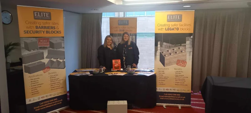 Two women at an exhibition stand with banners for barriers and security blocks