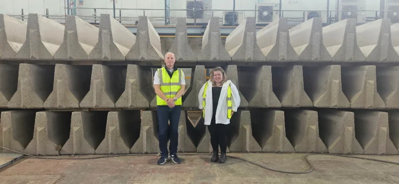 Two staff in hi-vis jackets standing in front of stacked precast concrete units