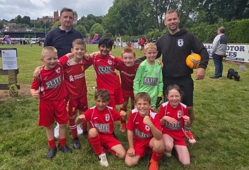 Junior football team in red kit with two coaches on a grass pitch