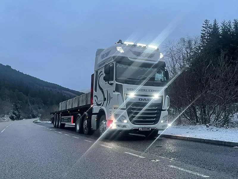 Articulated flatbed lorry travelling a rural road at dusk in winter