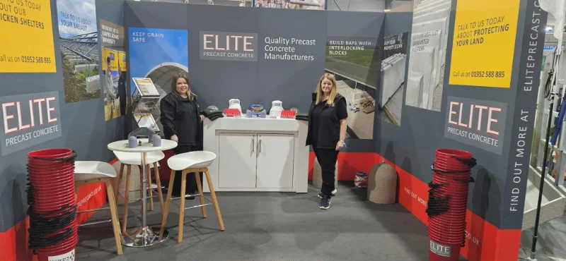 Two women staffing a branded exhibition stand with coiled pipe displays